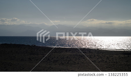 Golden hues reflect on calm waters during sunset near mountain range 138225355