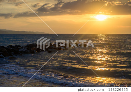 Romantic sunset scene on Cyprus shore with gentle sea breeze, orange sky, and silhouettes of rocks and palm trees. Romantic sunset scene on Cyprus shore with gentle sea breeze, orange sky, and silhouettes of rocks and palm trees. 138226335