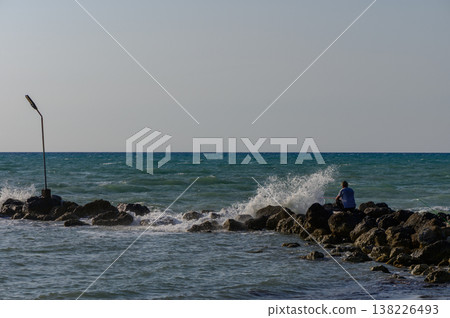 Man fishing on seaside rocks in Cyprus, casting his line into the clear Mediterranean waters under the sun. 138226493