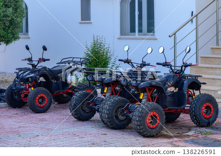 Three powerful black quad bikes parked side by side on a sunny day, ready for off-road adventure and travel. Three powerful black quad bikes parked side by side on a sunny day, ready for off-road adventure and travel. 138226591