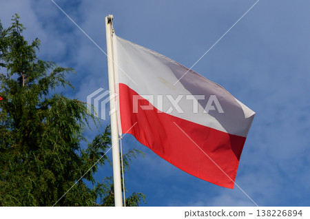 Polish flag waving proudly against a bright blue sky adorned with scattered clouds 138226894