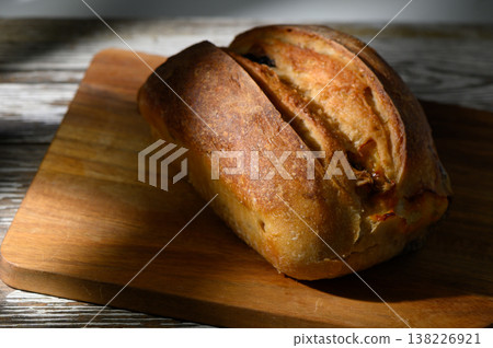 Freshly baked bread rests on a wooden cutting board under gentle afternoon light in a cozy kitchen setting Freshly baked bread rests on a wooden cutting board under gentle afternoon light in a cozy kitchen setting 138226921