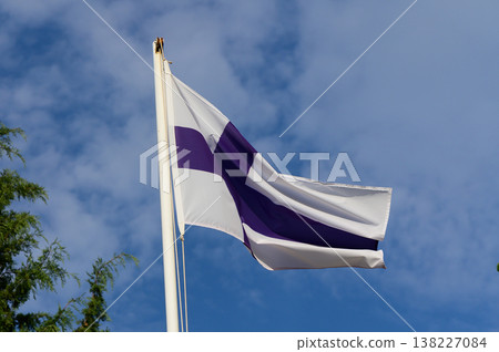 Finnish flag waving proudly against a bright blue sky, embraced by nature on a sunny day Finnish flag waving proudly against a bright blue sky, embraced by nature on a sunny day 138227084