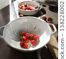 Fresh organic strawberries in white crackle glazed ceramic colander. High contrast photography of red berries on dark wood table with cinematic sunlight shadows and wabi-sabi aesthetic. 138228002