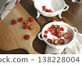 Fresh organic strawberries on wooden board and vintage ceramic bowls. Trendy rustic kitchen scene with red berries, white colander and sunlight shadows for healthy cottagecore lifestyle. 138228004