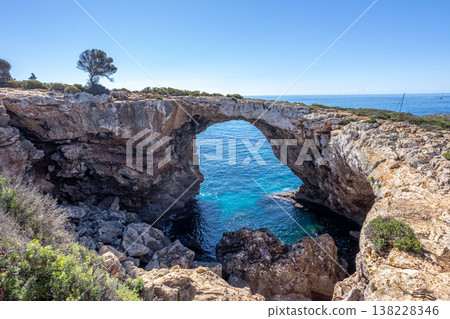 Scenic rocky arch forming a natural bridge above clear blue water at Cala Varques beach on Mallorca east coast under bright sunny sky 138228346