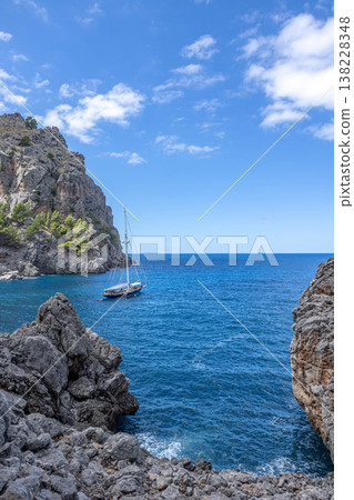 Peaceful coastal view with a sailboat floating on clear blue water surrounded by steep rocky cliffs near Sa Calobra on Mallorca west coast Peaceful coastal view with a sailboat floating on clear blue water surrounded by steep rocky cliffs near Sa Calobra on Mallorca west coast 138228348