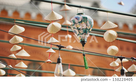Traditional Asian decorations with conical hats and a floral lantern hanging at an outdoor festival. Traditional Asian decorations with conical hats and a floral lantern hanging at an outdoor festival. 138228405