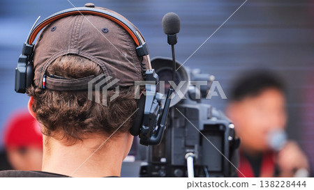 Cameraman wearing a headset with a microphone operating a video camera during an event. 138228444