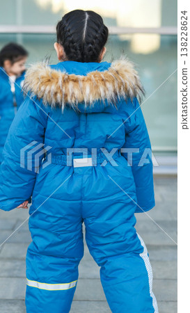 Little girl wearing warm blue snowsuit with faux fur hood walking outdoors Little girl wearing warm blue snowsuit with faux fur hood walking outdoors 138228624