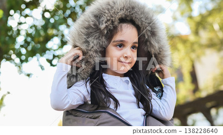 Smiling little girl wearing a warm winter coat with faux fur hood outdoors Smiling little girl wearing a warm winter coat with faux fur hood outdoors 138228640