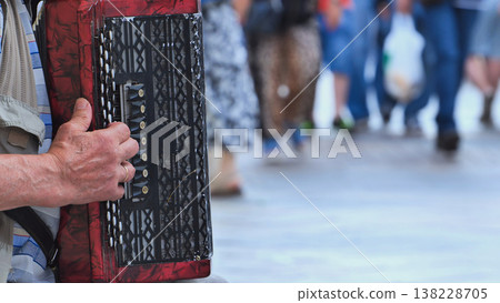 Street musician playing accordion, entertaining passersby in urban outdoor scene 138228705