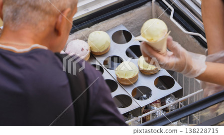 Customer buying ice cream cone from vendor at outdoor freezer in summer 138228715