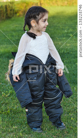 Little girl playing outdoors, wearing oversized black snowsuit for humor and fun Little girl playing outdoors, wearing oversized black snowsuit for humor and fun 138228746