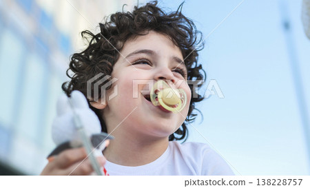 Happy toddler boy with curly hair smiling and playing with a toy outdoors Happy toddler boy with curly hair smiling and playing with a toy outdoors 138228757
