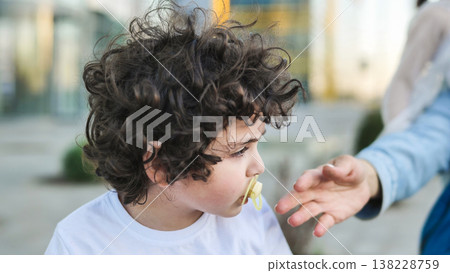 Boy with curly hair and pacifier extending hand towards an adult's outstretched arm 138228759