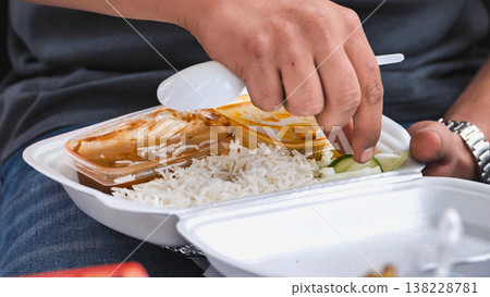 Hand scooping curry and rice from a white styrofoam container, enjoying a meal 138228781