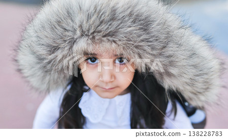 Little girl wearing a fur hood looking directly at camera outdoors in winter Little girl wearing a fur hood looking directly at camera outdoors in winter 138228783