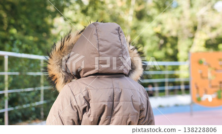 Child wearing warm fur hood jacket, staying active in a playground outdoors 138228806