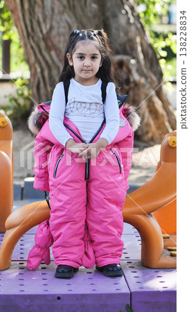 Child standing on playground wearing pink snowsuit, looking at camera Child standing on playground wearing pink snowsuit, looking at camera 138228834