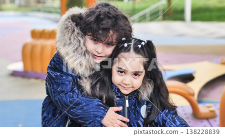 Siblings sharing a warm hug and connection, playing at the park in winter coats 138228839