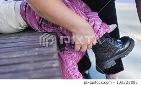 Parent helping child wearing warm clothes and leopard print boots outdoors 138228895