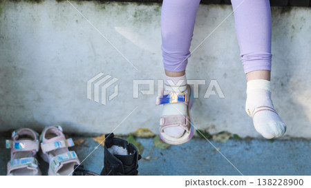 Child's legs dangling with colorful sandals and socks, choosing footwear outdoors Child's legs dangling with colorful sandals and socks, choosing footwear outdoors 138228900