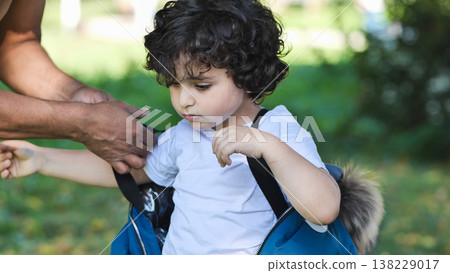 Father helping young curly-haired boy putting on jacket outdoors, parenting care 138229017