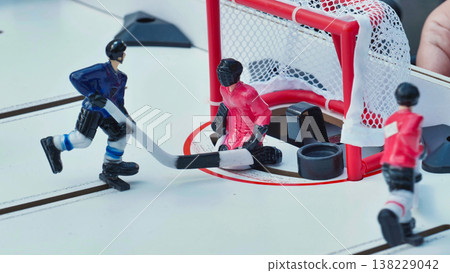 Table hockey game with blue player shooting on a red goalie at the net. 138229042