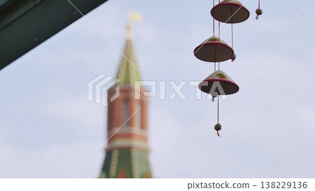 Decorative hanging bells with a historic tower blurred in the background against a pale sky. 138229136