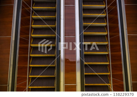 Escalators moving up and down in modern building interior, creating parallel lines 138229370