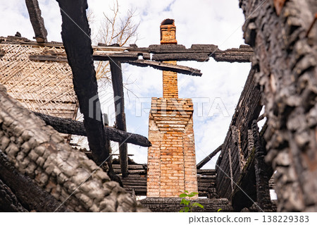 Burnt house remains with a brick chimney standing amidst charred timbers Burnt house remains with a brick chimney standing amidst charred timbers 138229383