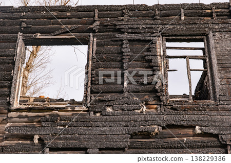 Burnt house wall with charred wooden logs and empty windows after fire disaster Burnt house wall with charred wooden logs and empty windows after fire disaster 138229386