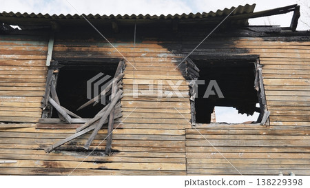 Burnt house facade showing fire damage, charred wood, and broken windows Burnt house facade showing fire damage, charred wood, and broken windows 138229398