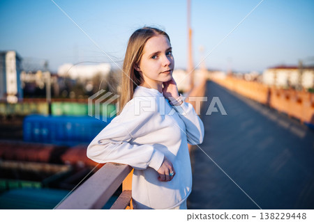 Young girl relaxing on city bridge at sunset, enjoying urban outdoor lifestyle Young girl relaxing on city bridge at sunset, enjoying urban outdoor lifestyle 138229448