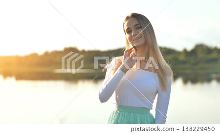 Young woman smiling, enjoying golden sunset hour by peaceful lake Young woman smiling, enjoying golden sunset hour by peaceful lake 138229450