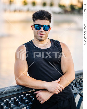 Young man with athletic physique wearing blue sunglasses outdoors Young man with athletic physique wearing blue sunglasses outdoors 138229481
