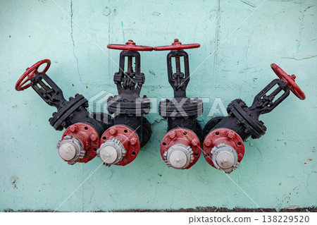 Four red and black industrial valves mounted on a turquoise concrete wall 138229520