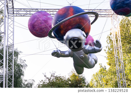 Astronaut sculpture flying through cosmic outdoor display with colorful planets 138229528