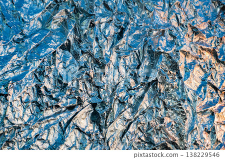 Crumpled aluminum foil texture creating an abstract metallic background with blue light 138229546