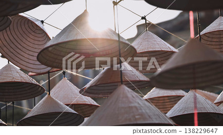 Traditional Asian conical hats hanging outdoors against a bright sun Traditional Asian conical hats hanging outdoors against a bright sun 138229647