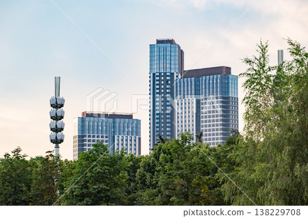 Modern city skyline with multiple high-rises rising above lush green treeline 138229708