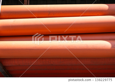 Stacked orange PVC pipes creating an abstract pattern with light and shadow Stacked orange PVC pipes creating an abstract pattern with light and shadow 138229775