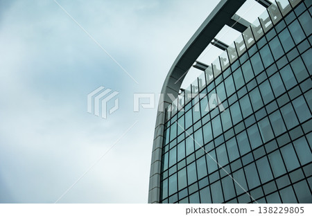 Modern glass facade curving against clear sky showcasing contemporary architecture Modern glass facade curving against clear sky showcasing contemporary architecture 138229805