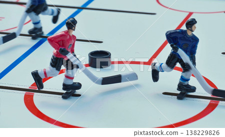 Miniature table hockey game with red and blue players competing for the puck on an ice rink. 138229826