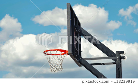 Basketball hoop and backboard against a bright blue sky with clouds 138229919