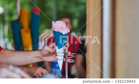 An ice cream vendor scoops ice cream into colorful waffle cones. 138229942