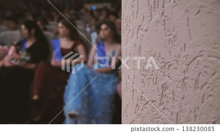 Graduates celebrating academic success, sitting together in crowded auditorium, wearing graduation gowns and sharing collective excitement Graduates celebrating academic success, sitting together in crowded auditorium, wearing graduation gowns and sharing collective excitement 138230085