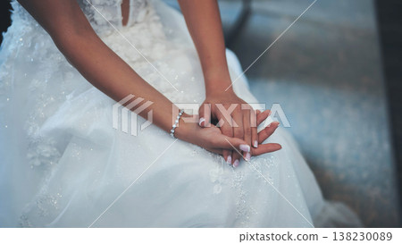 White glittering wedding dress highlighting delicate bride's hand, displaying elegant bracelet and sparkling ring White glittering wedding dress highlighting delicate bride's hand, displaying elegant bracelet and sparkling ring 138230089