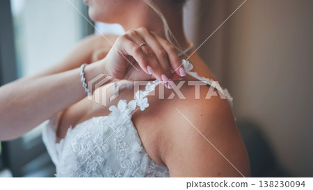 Close up of a bride adjusting the strap of her lace wedding gown, showing her hand with ring and bracelet. Close up of a bride adjusting the strap of her lace wedding gown, showing her hand with ring and bracelet. 138230094